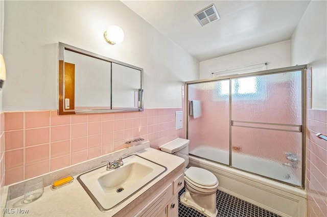 full bathroom with combined bath / shower with glass door, tile walls, vanity, toilet, and tile patterned floors