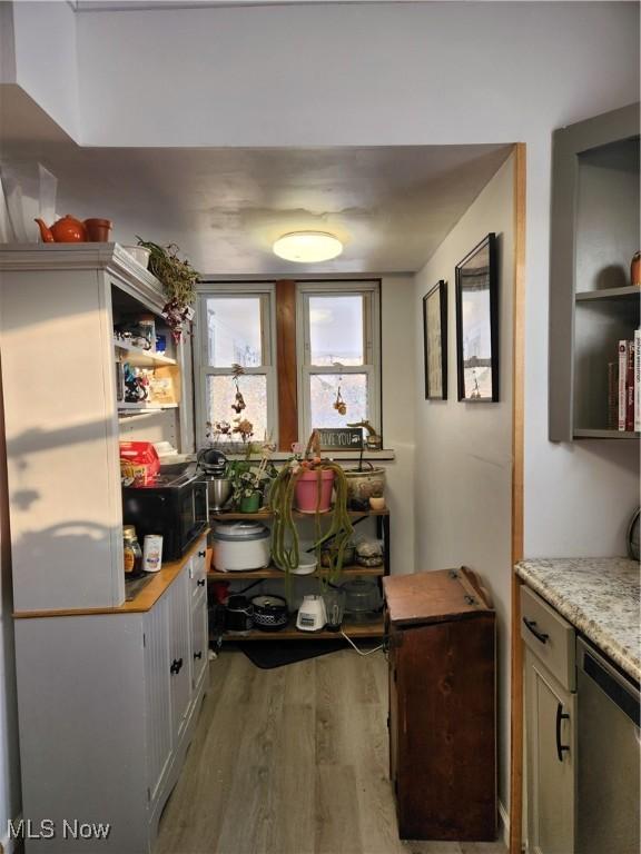 kitchen featuring light stone countertops, hardwood / wood-style flooring, and stainless steel dishwasher