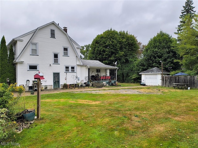 rear view of property with a garage, an outdoor structure, a porch, and a lawn