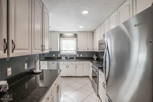 kitchen with sink, stainless steel appliances, white cabinets, light tile patterned flooring, and dark stone counters