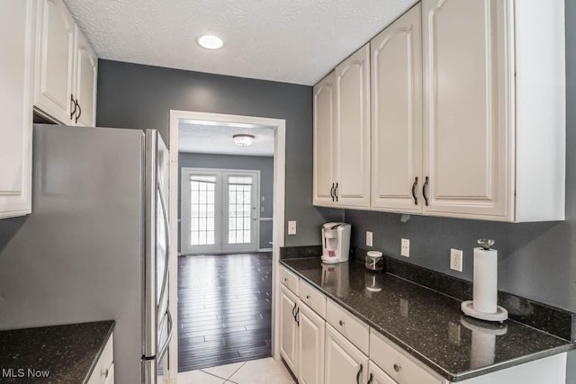 kitchen with white cabinets, dark stone countertops, stainless steel fridge, and a textured ceiling