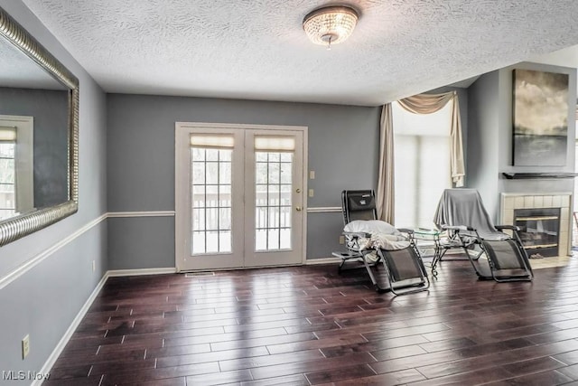 sitting room with dark wood-type flooring, a tiled fireplace, and a textured ceiling