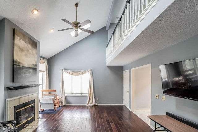 living area with wood finished floors, baseboards, ceiling fan, a textured ceiling, and a tiled fireplace