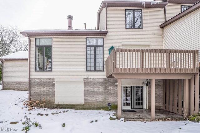 snow covered rear of property featuring french doors, a balcony, and brick siding