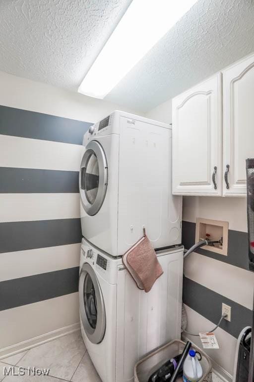 clothes washing area featuring light tile patterned floors, cabinets, a textured ceiling, and stacked washer / dryer