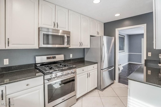 kitchen featuring white cabinetry, light tile patterned floors, stainless steel appliances, and dark stone countertops