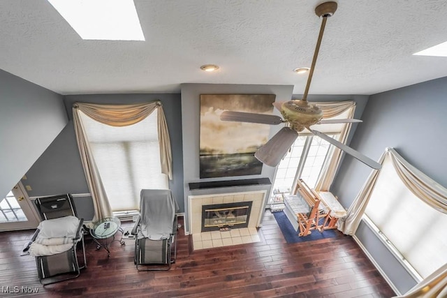 sitting room featuring dark hardwood / wood-style flooring, a skylight, a tile fireplace, and a textured ceiling