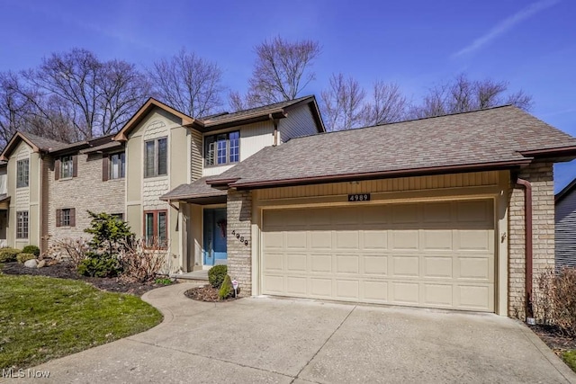 traditional home featuring brick siding, an attached garage, driveway, and roof with shingles