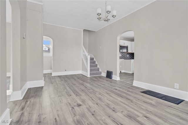 unfurnished living room with light hardwood / wood-style flooring, ornamental molding, and a chandelier