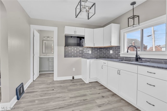 kitchen featuring pendant lighting, sink, white cabinetry, backsplash, and light wood-type flooring