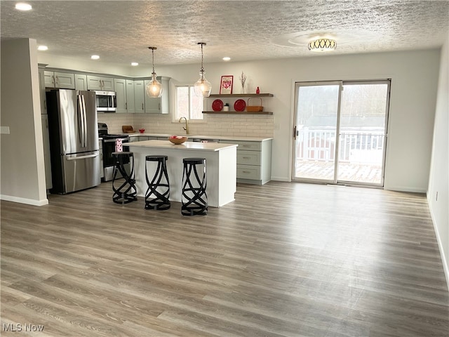 kitchen with appliances with stainless steel finishes, wood finished floors, a center island, and light countertops