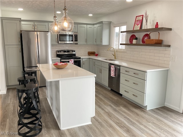 kitchen featuring sink, a center island, light wood-type flooring, appliances with stainless steel finishes, and pendant lighting