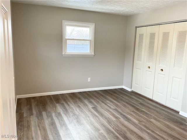 unfurnished bedroom featuring dark wood-type flooring, a textured ceiling, and a closet