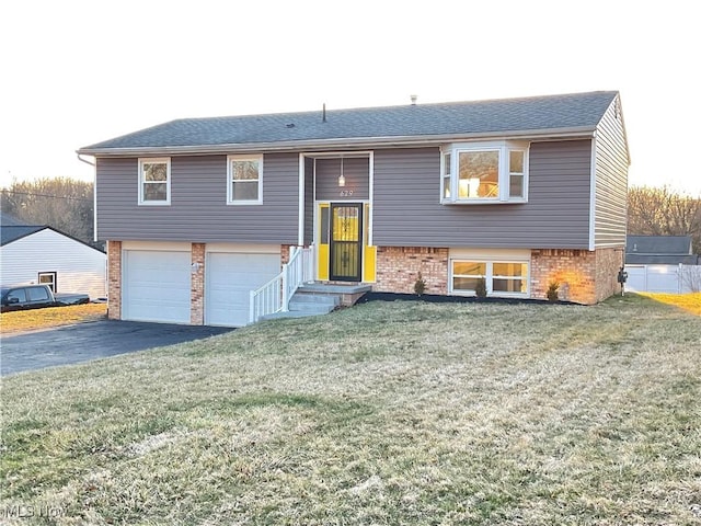 split foyer home featuring driveway, a shingled roof, a front lawn, a garage, and brick siding