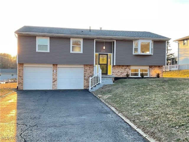 split foyer home with brick siding, a shingled roof, a front lawn, aphalt driveway, and an attached garage