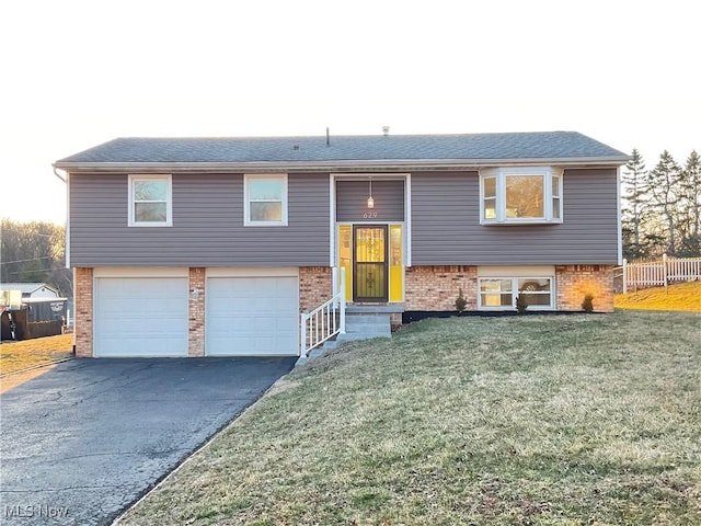 split foyer home featuring brick siding, an attached garage, fence, a front yard, and driveway