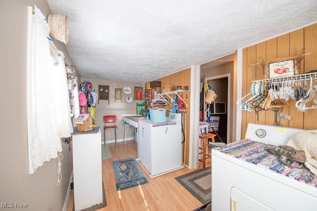 clothes washing area with washer / dryer, a textured ceiling, light hardwood / wood-style floors, and wood walls