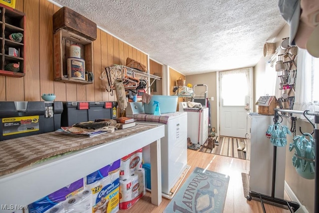 laundry area with wooden walls, washer / dryer, light hardwood / wood-style flooring, and a textured ceiling