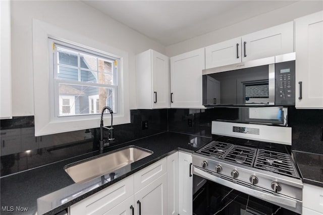 kitchen with sink, white cabinetry, dark stone counters, stainless steel appliances, and backsplash