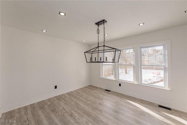 unfurnished dining area featuring an inviting chandelier and light hardwood / wood-style floors