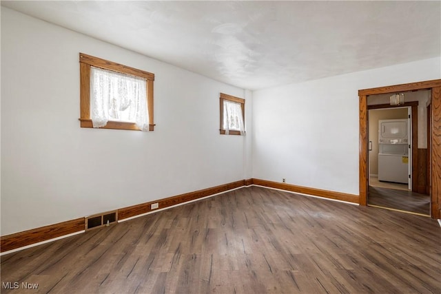 empty room with stacked washing maching and dryer and dark hardwood / wood-style flooring