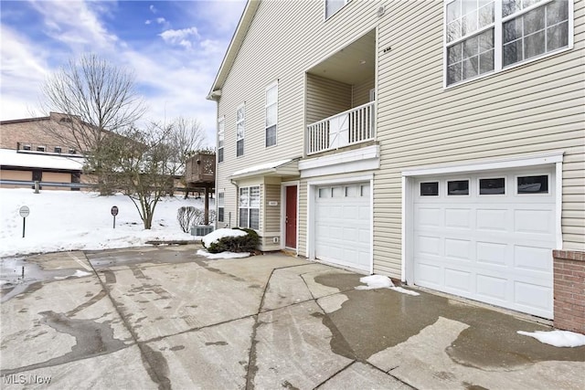 view of snowy exterior featuring a garage, a balcony, and central air condition unit