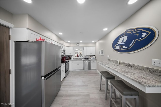 kitchen with a kitchen bar, sink, light stone counters, appliances with stainless steel finishes, and white cabinets