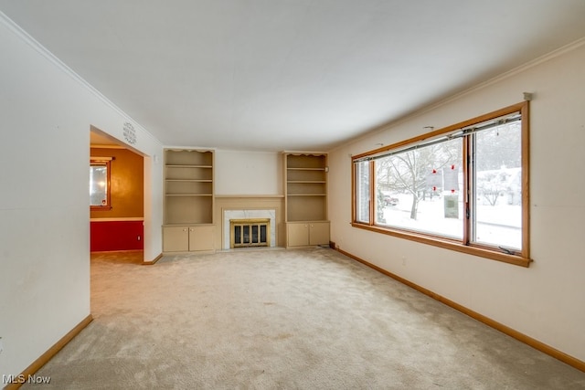 unfurnished living room with built in shelves, a high end fireplace, ornamental molding, and carpet flooring