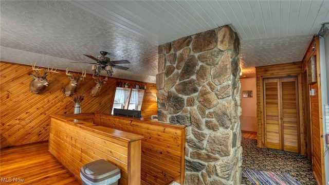 bar with ceiling fan, hardwood / wood-style floors, a textured ceiling, and wood walls