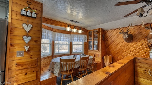 dining area featuring vaulted ceiling, hardwood / wood-style floors, wood walls, ceiling fan, and a textured ceiling