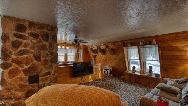 carpeted living room with ceiling fan, wooden walls, and a textured ceiling