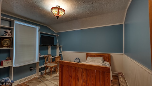 bedroom with vaulted ceiling, a textured ceiling, and light hardwood / wood-style flooring