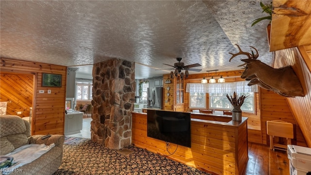 living room featuring wood-type flooring, ceiling fan, a textured ceiling, and wooden walls