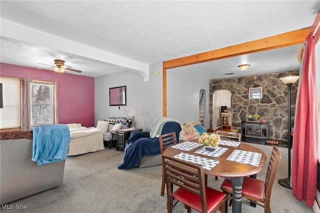 carpeted dining room featuring beam ceiling, a textured ceiling, ceiling fan, and a wood stove