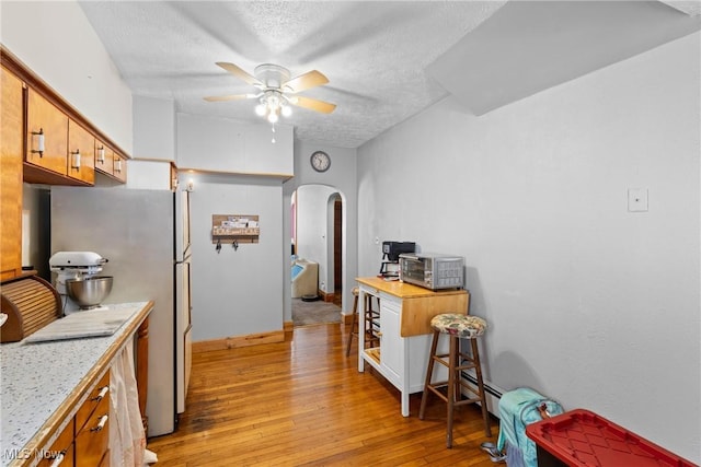 kitchen with stainless steel refrigerator, a textured ceiling, ceiling fan, and light hardwood / wood-style flooring