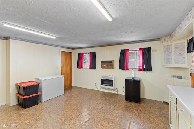 basement featuring fridge, heating unit, and a textured ceiling