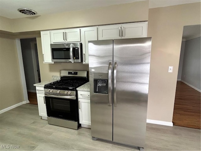 kitchen with light stone counters, stainless steel appliances, light hardwood / wood-style floors, and white cabinets