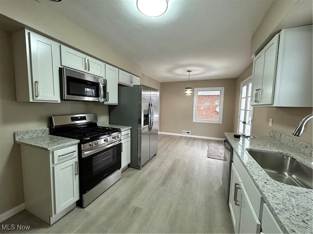 kitchen featuring sink, white cabinetry, hanging light fixtures, stainless steel appliances, and light stone counters