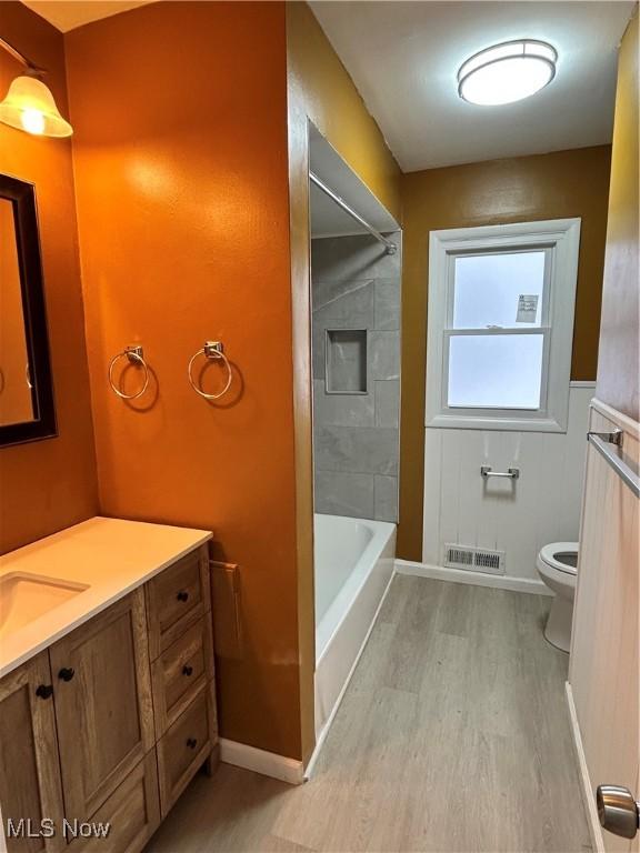 full bathroom with tiled shower / bath, wood-type flooring, toilet, and vanity