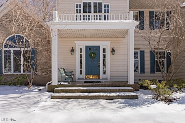 snow covered property entrance featuring a balcony and a porch