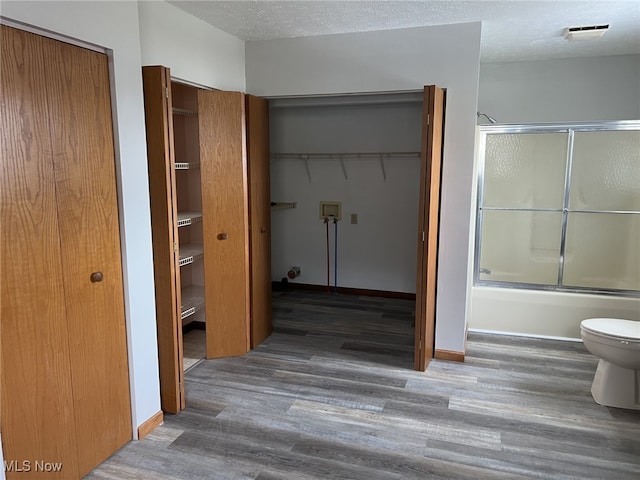 bathroom with hardwood / wood-style floors, toilet, enclosed tub / shower combo, and a textured ceiling