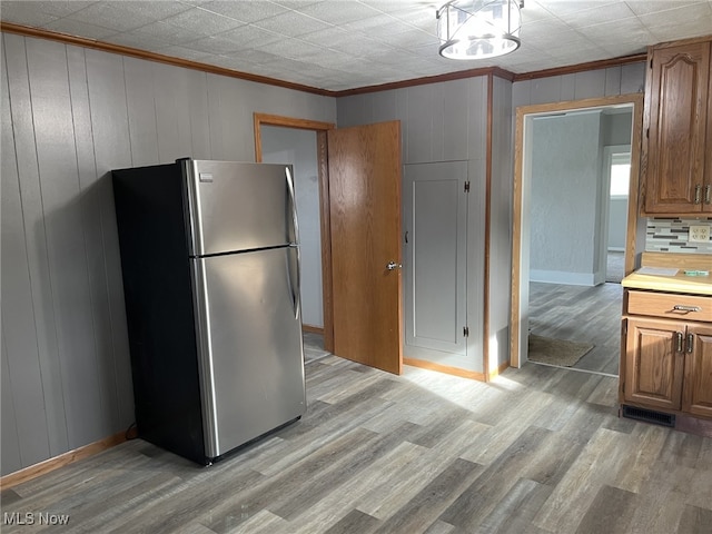 kitchen with ornamental molding, wooden walls, stainless steel fridge, and light wood-type flooring