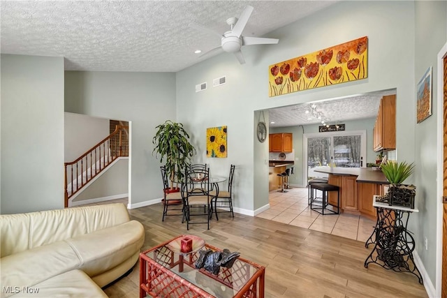 living room with ceiling fan, a towering ceiling, a textured ceiling, and light wood-type flooring