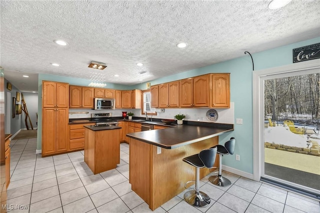 kitchen with appliances with stainless steel finishes, a kitchen bar, a center island, light tile patterned floors, and kitchen peninsula