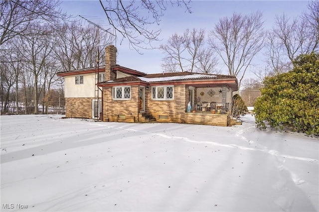 snow covered back of property featuring covered porch