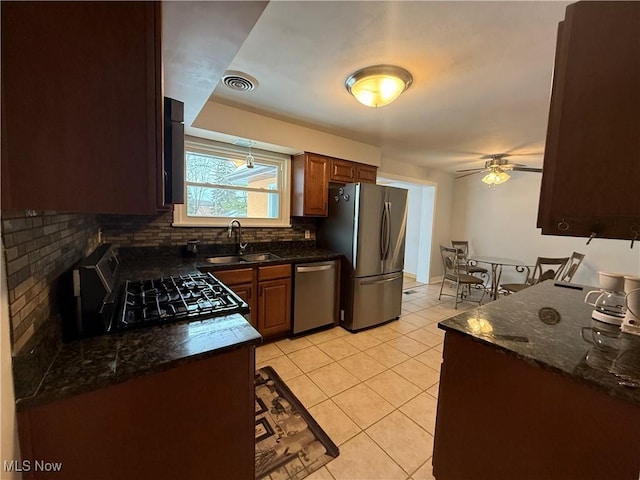 kitchen with light tile patterned flooring, appliances with stainless steel finishes, sink, decorative backsplash, and dark stone counters