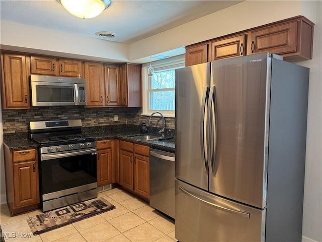 kitchen with sink, tasteful backsplash, light tile patterned floors, dark stone counters, and stainless steel appliances