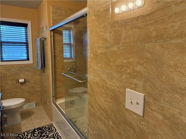 bathroom with toilet, tile patterned flooring, combined bath / shower with glass door, and tile walls