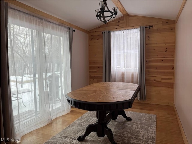 dining space with vaulted ceiling with beams, a chandelier, light hardwood / wood-style floors, and wood walls