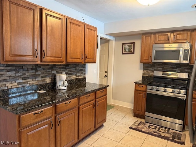 kitchen with dark stone countertops, light tile patterned floors, decorative backsplash, and appliances with stainless steel finishes